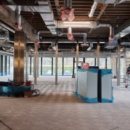 Southwell Group - Wnętrze komercyjne w trakcie prac wykończeniowych: widoczne instalacje wentylacyjne pod sufitem, metalowe kolumny, rusztowania i materiały budowlane na podłodze.