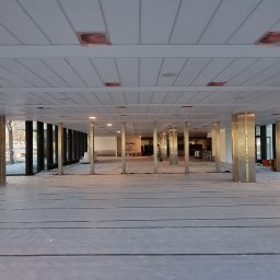 Southwell Group - Przestronne wnętrze biurowe w trakcie prac wykończeniowych: zabezpieczona podłoga, metalowe kolumny, rusztowanie. Widoczne okna i sufit z oświetleniem.