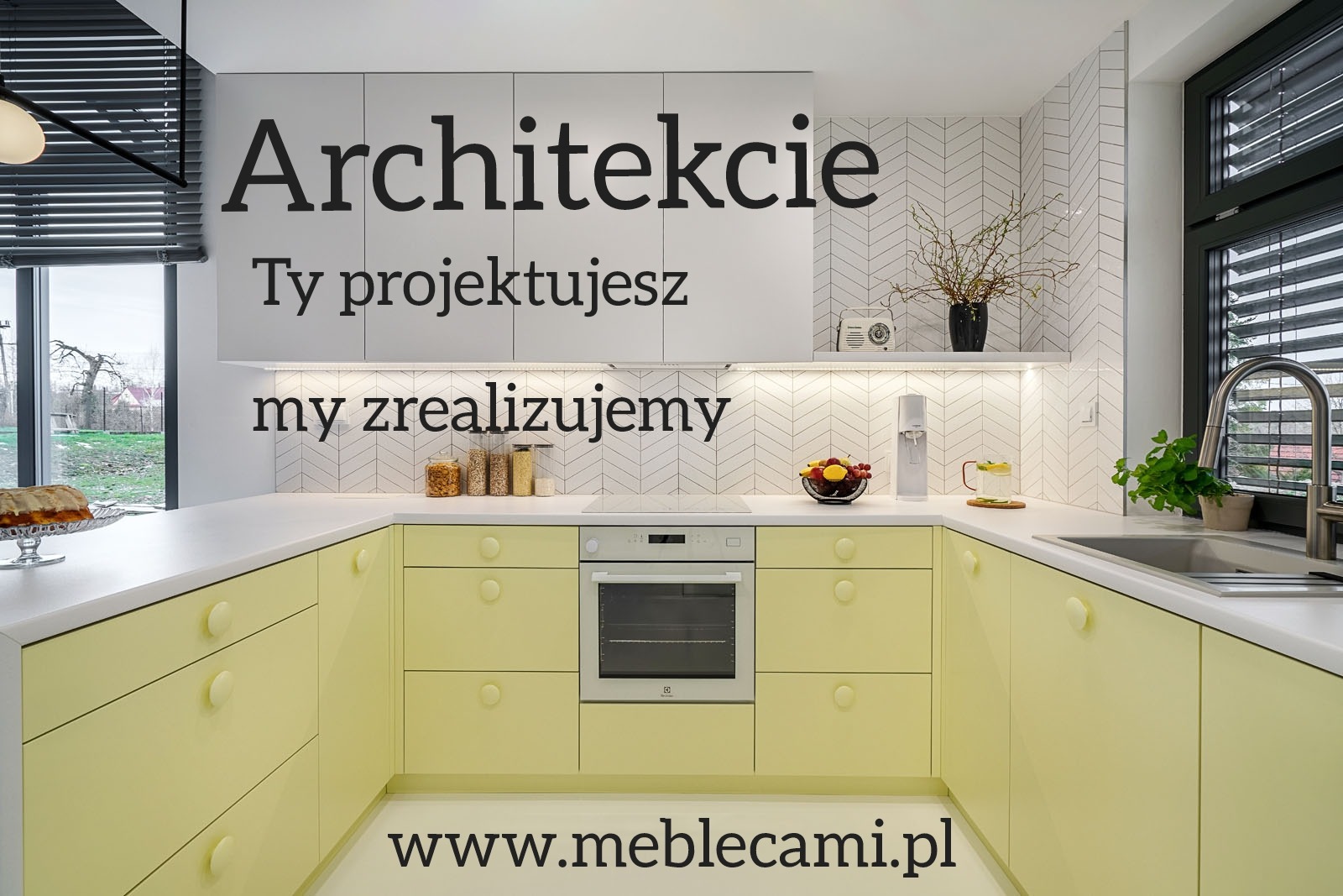 Żółta kuchnia w kształcie litery U z białym blatem i szafkami wiszącymi. Na blacie owoce, radio i roślina. Nadruk z hasłem 'Architekcie Ty projektujesz my zrealizujemy'.