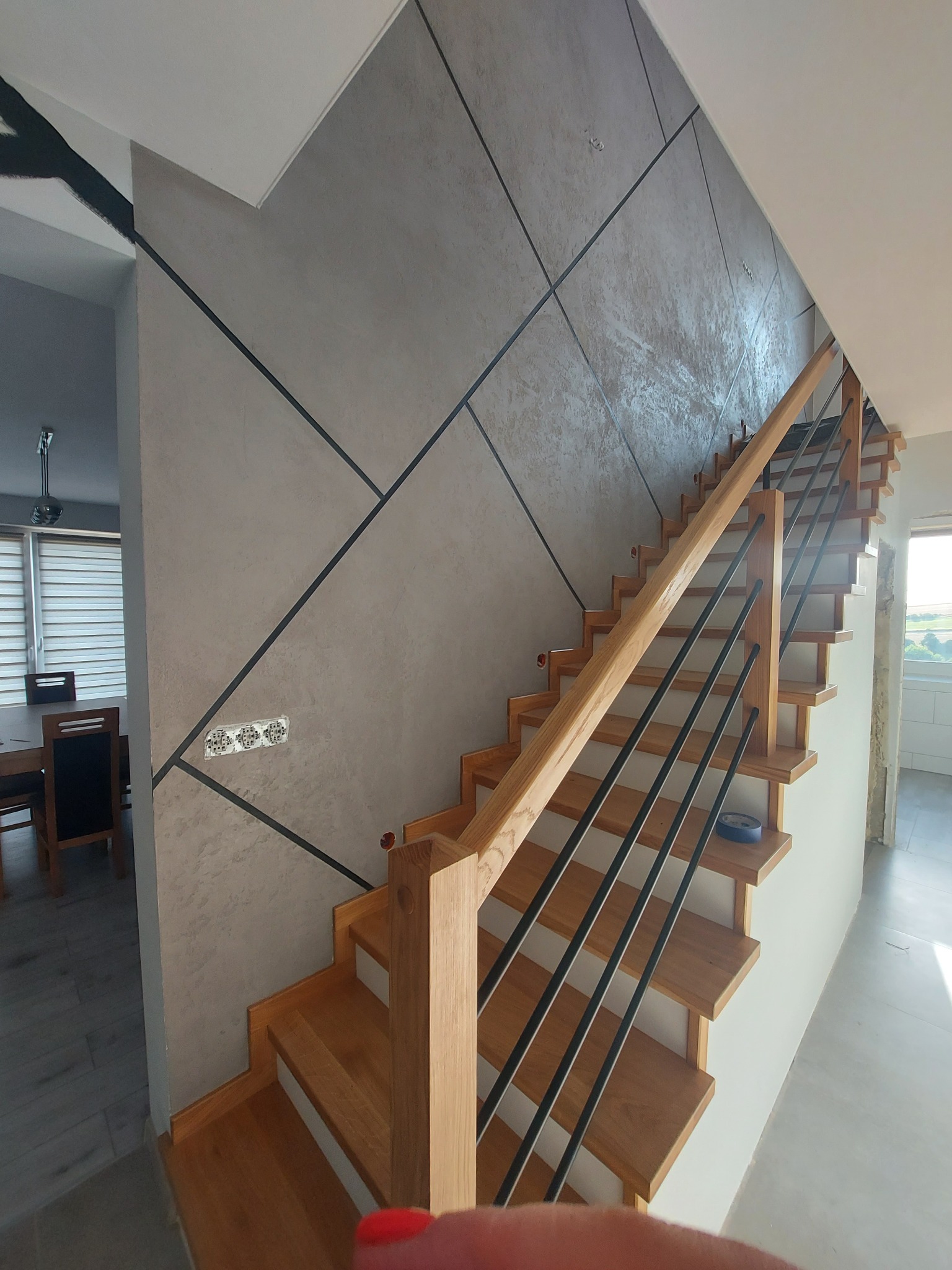 Ściana z dekoracyjnym tynkiem w geometryczne wzory, drewniane schody z czarnymi balustradami. Wykończenie wnętrza w nowoczesnym stylu.