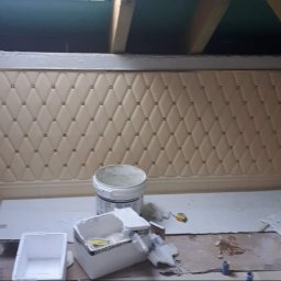 DUM - BUD ANDRZEJ DUMANOWSKI - Beżowa, pikowana ściana w skosie poddasza z dekoracyjnymi guzikami. Widoczne narzędzia i materiały budowlane. Prace wykończeniowe w trakcie realizacji.