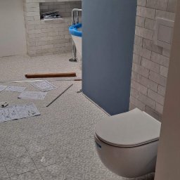 Dum-bud Dumanowski Andrzej - Ukończona łazienka na poddaszu z wzorzystą podłogą, białą armaturą i niebieską ścianą. Widoczne plany i narzędzia na podłodze, co sugeruje świeży remont.