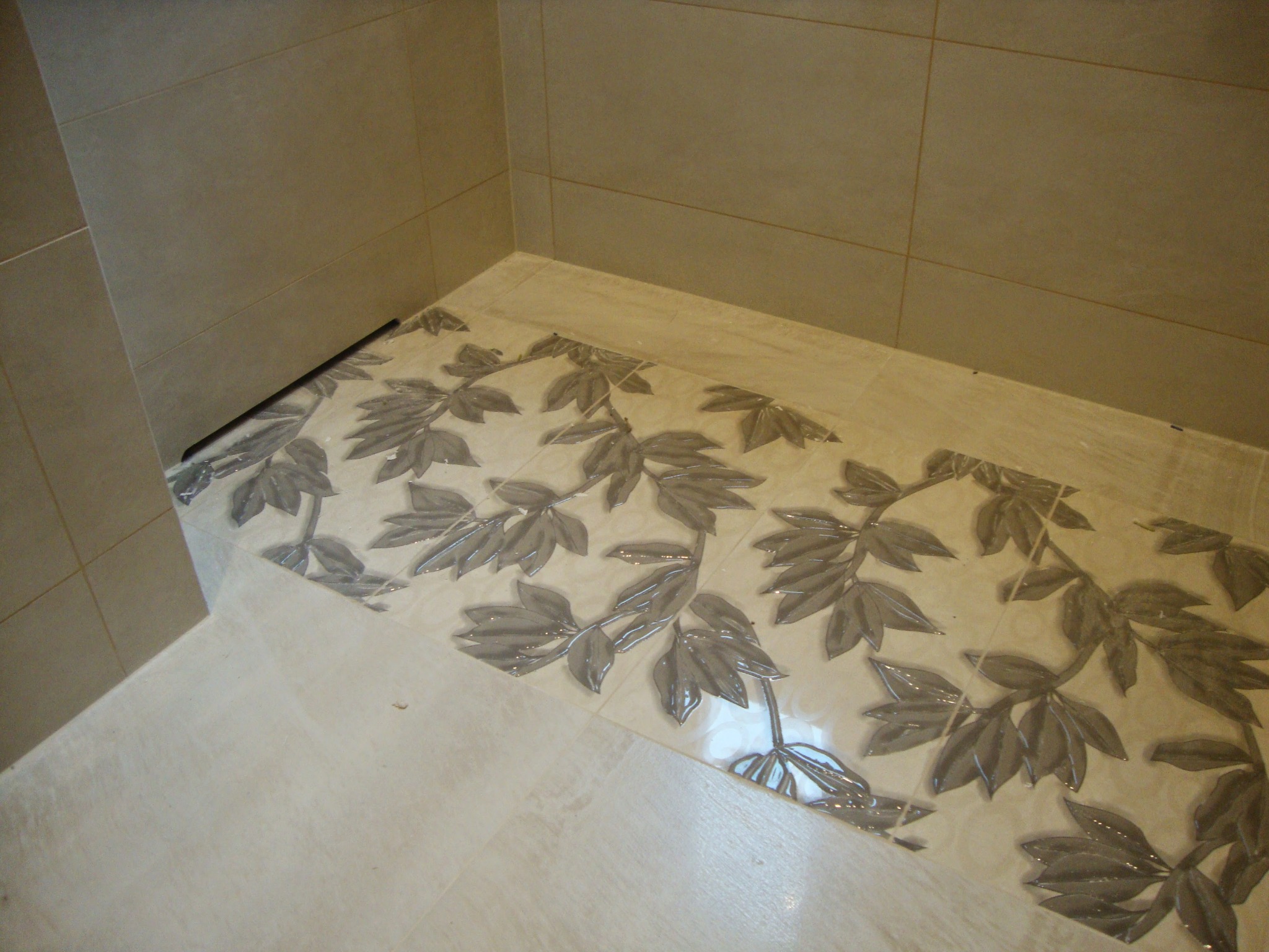 Beżowe płytki ścienne i podłogowe z motywem liści w łazience. Ukończona aranżacja z detalami, widok z góry, neutralne oświetlenie.