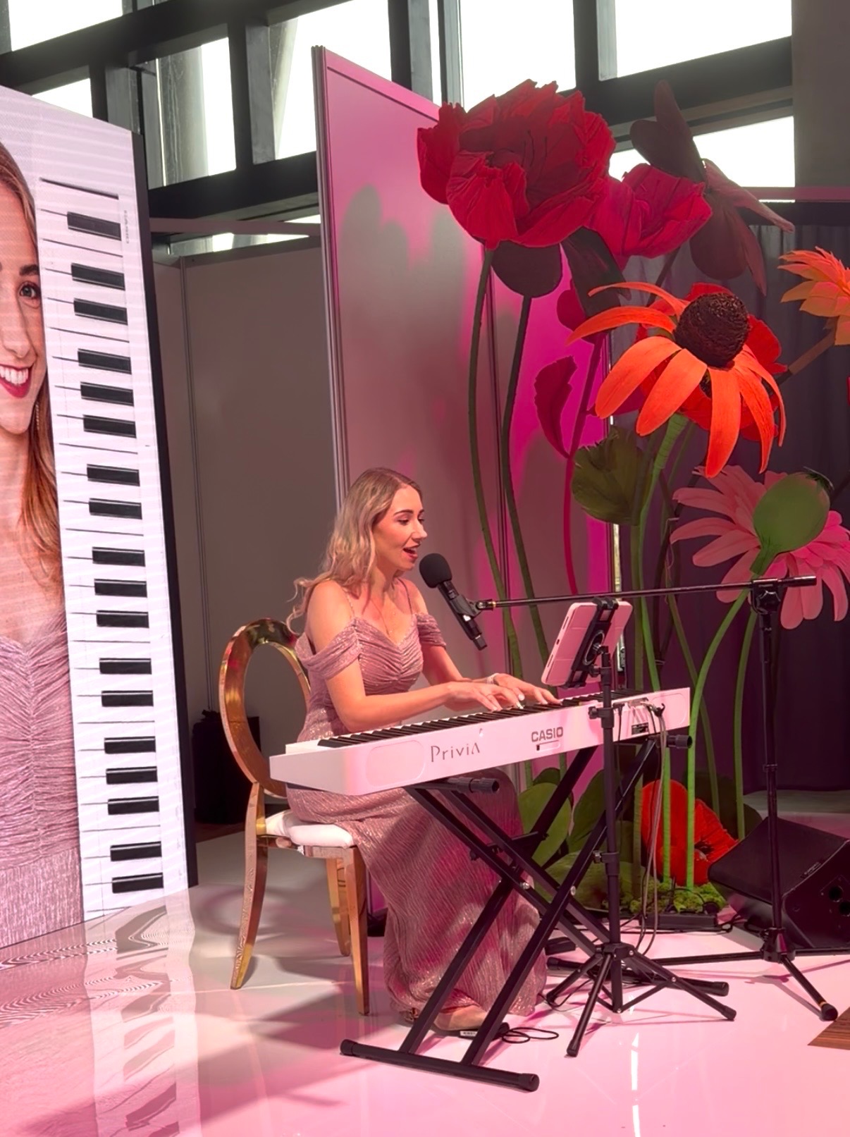 Wokalistka grająca na keyboardzie Casio Privia podczas występu we Wrocławiu. W tle dekoracje kwiatowe i ekran z wizerunkiem artystki.
