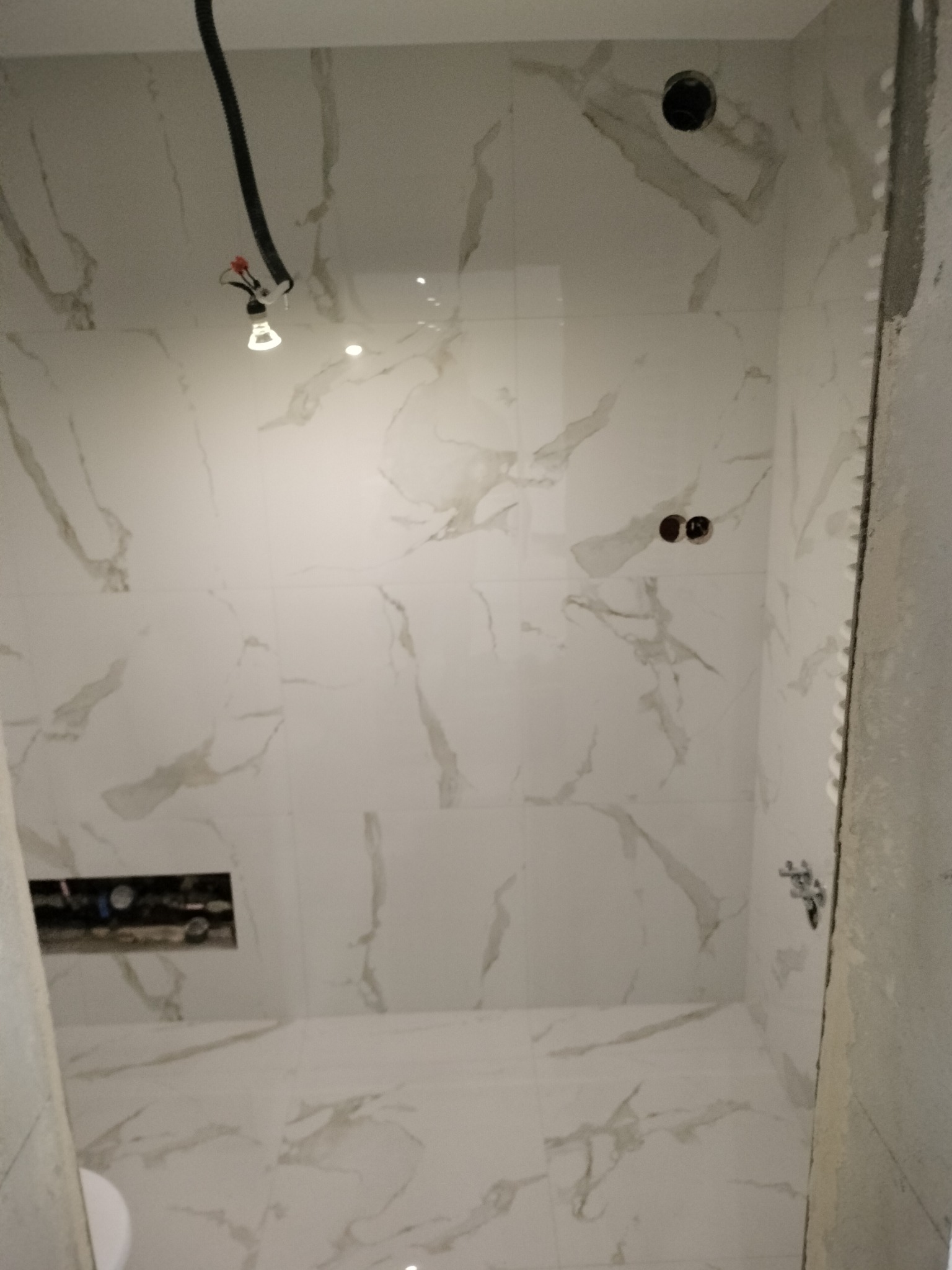 Wykończona łazienka w Topólce z białymi płytkami imitującymi marmur. Widoczne punkty instalacji wodnej i elektrycznej, gotowe do montażu armatury.