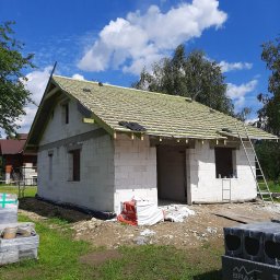 Usługi Ogólnobudowlane Jawor Mateusz Jaworski - Budowa domu w trakcie: białe bloczki, drewniana konstrukcja dachu z łatami, drabina oparta o ścianę. Częściowo ułożone dachówki. Materiały budowlane na pierwszym planie.