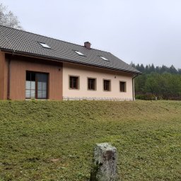 Usługi Ogólnobudowlane Jawor Mateusz Jaworski - Dwukondygnacyjny dom z brązowymi oknami i dachem z dachówki, otoczony świeżo skoszoną trawą i drzewami w tle, widziany z niskiego kąta.