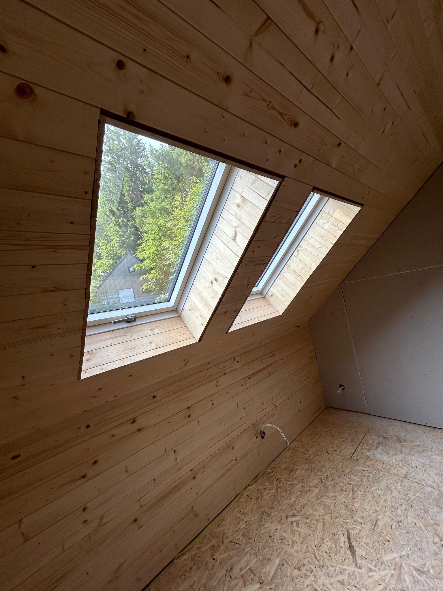 Drewniane wykończenie poddasza z oknami dachowymi w Trzebieszowicach. Widok na zewnątrz przez okna. Część ściany wykończona płytą karton gips.