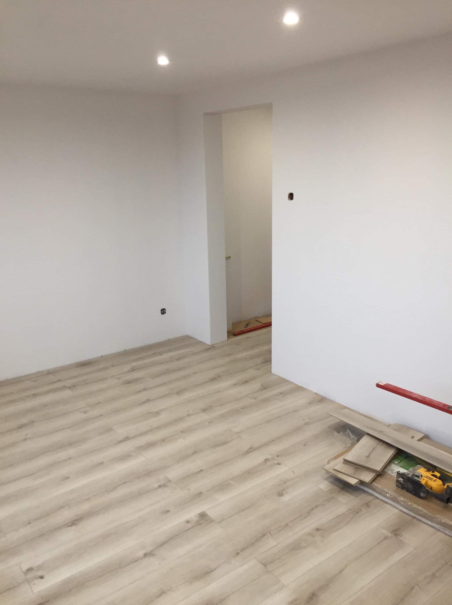 Ułożona podłoga z paneli w jasnym odcieniu drewna w Kartuzach. Widoczne narzędzia i resztki paneli. Świeżo wyremontowane wnętrze z białymi ścianami i punktowym oświetleniem.