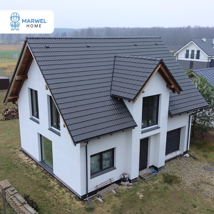 Nowoczesny, dwukondygnacyjny dom z ciemnoszarą dachówką, białymi ścianami i dużymi oknami. Widok z góry ukazuje bryłę budynku i otoczenie.