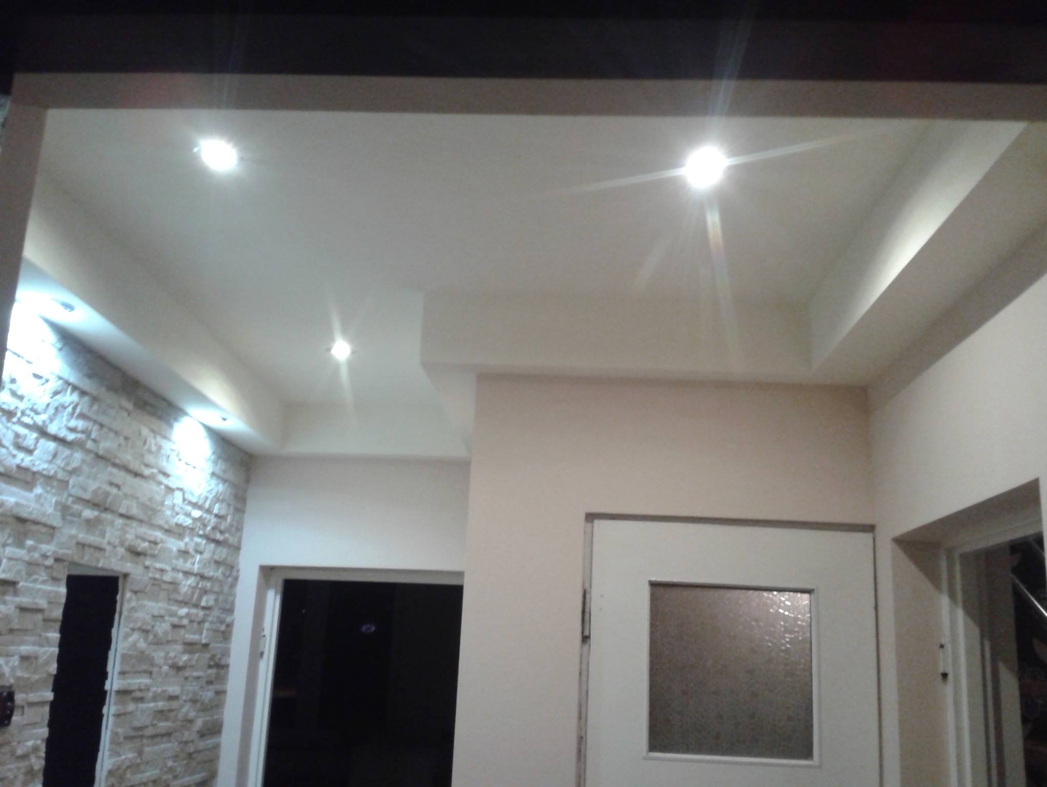 Wykończone wnętrze z podwieszanym sufitem z oświetleniem punktowym, ściana z dekoracyjną okładziną imitującą kamień i białe drzwi z szybą.