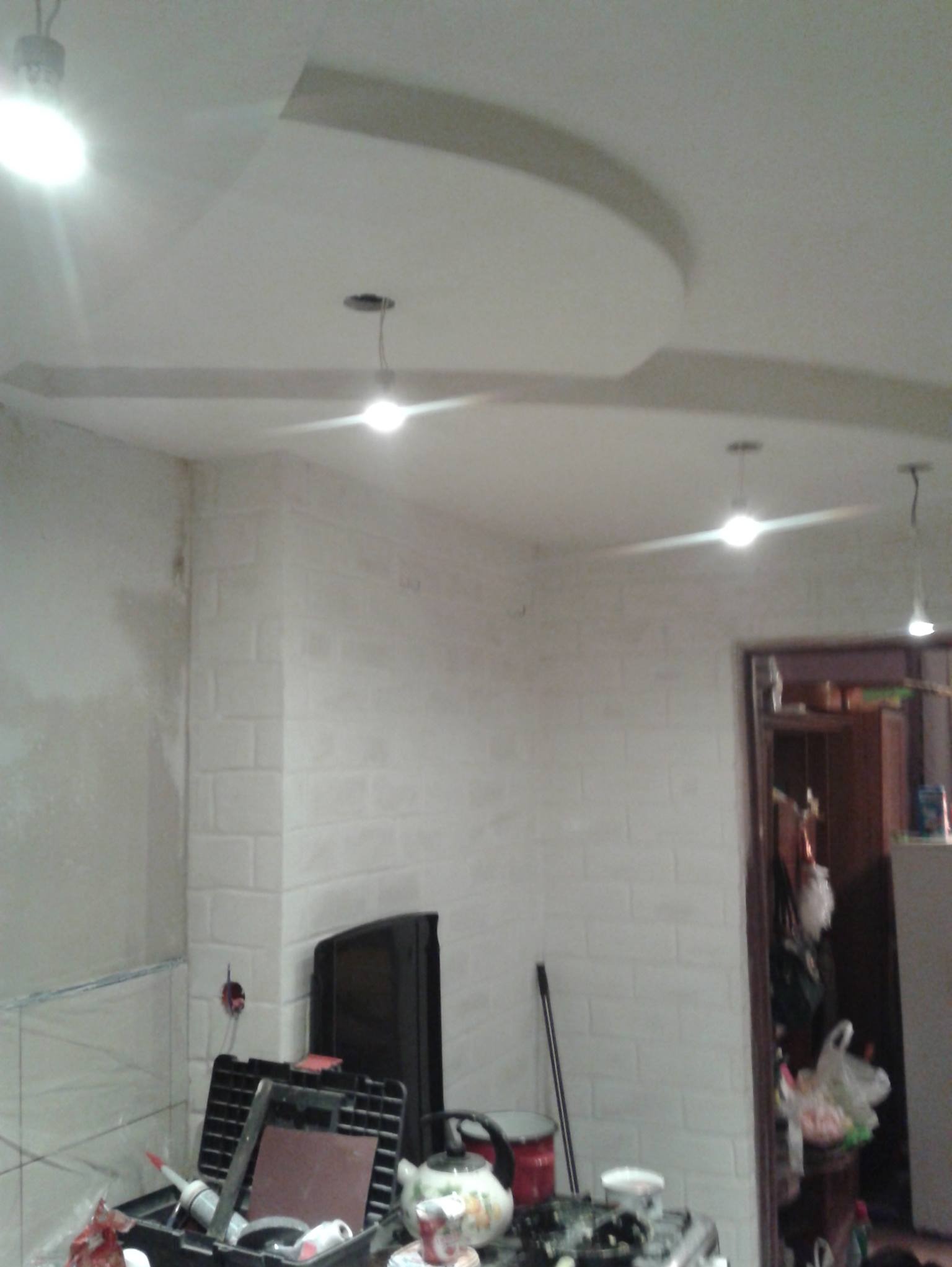 Remont wnętrza: ściana wyłożona białą cegłą, sufit z podwieszanym elementem i oświetleniem. Widoczne narzędzia i akcesoria remontowe.