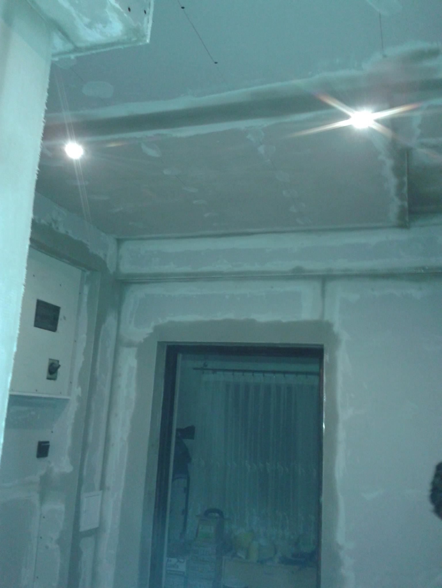 Wnętrze w trakcie prac wykończeniowych: ściany i sufit pokryte gładzią gipsową, widoczne punkty oświetleniowe i przygotowane otwory na instalacje.