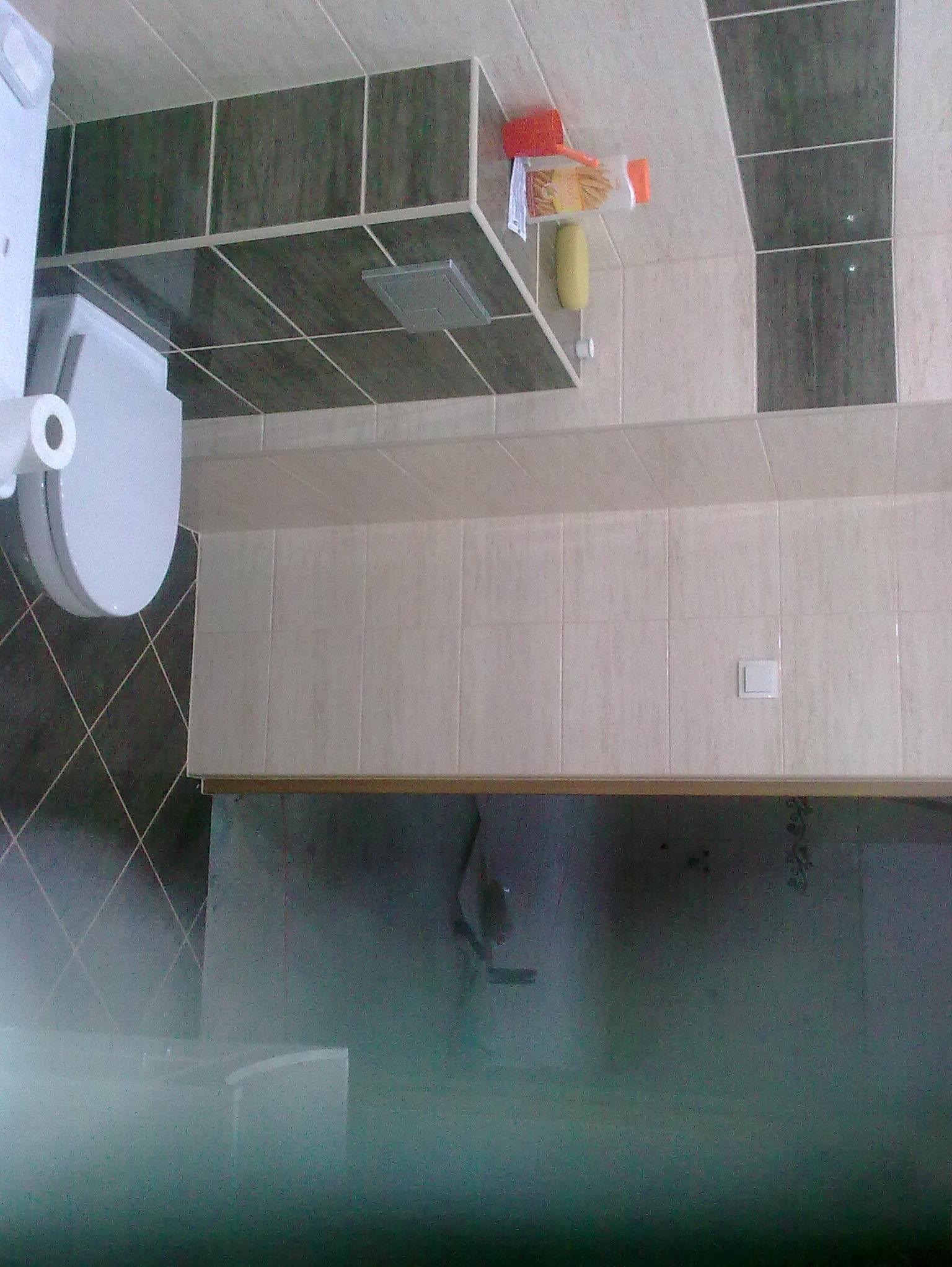 Wykończona łazienka z toaletą, umywalką i glazurą w odcieniach beżu i szarości. Na ścianie widoczne akcesoria łazienkowe i włącznik światła.