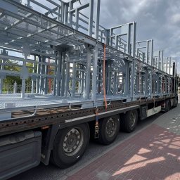 Malar - Konstrukcja stalowa, prawdopodobnie balkonowa, zabezpieczona pasami transportowymi na naczepie ciężarówki, gotowa do montażu. Widok z boku, pochmurne niebo w tle.
