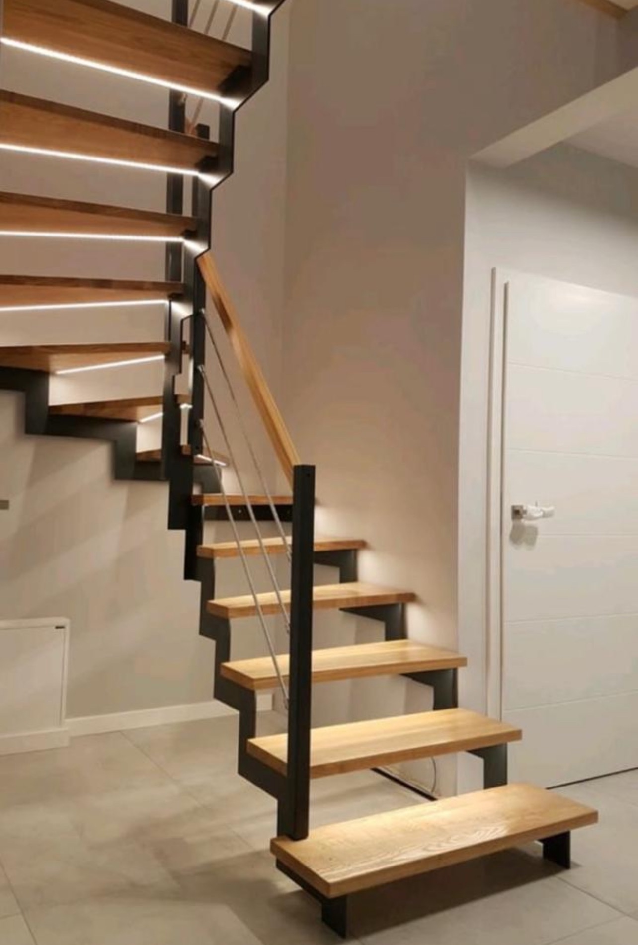 Nowoczesne schody metalowe z drewnianymi stopniami i podświetleniem LED, minimalistyczny design, jasne wnętrze, widok z dołu, eleganckie wykończenie.