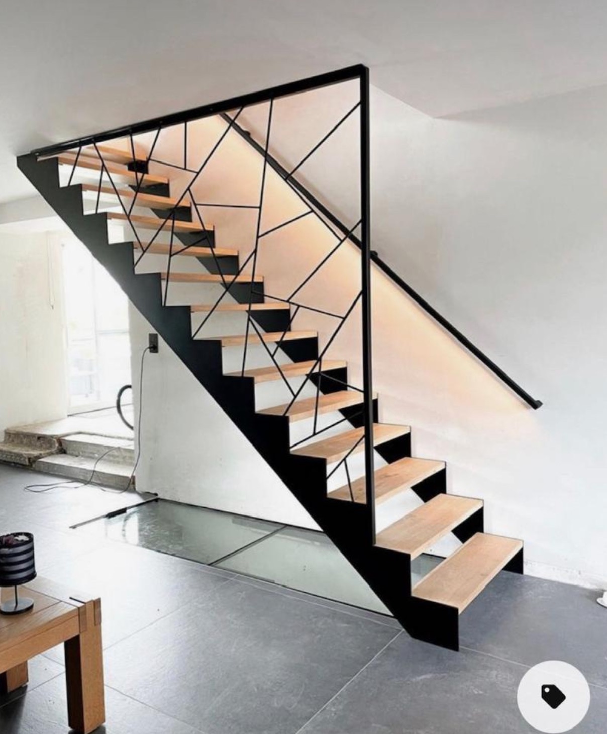 Nowoczesne schody z drewnianymi stopniami i czarną, geometryczną balustradą. Minimalistyczny design, jasne wnętrze, widoczne niedokończone prace w tle.