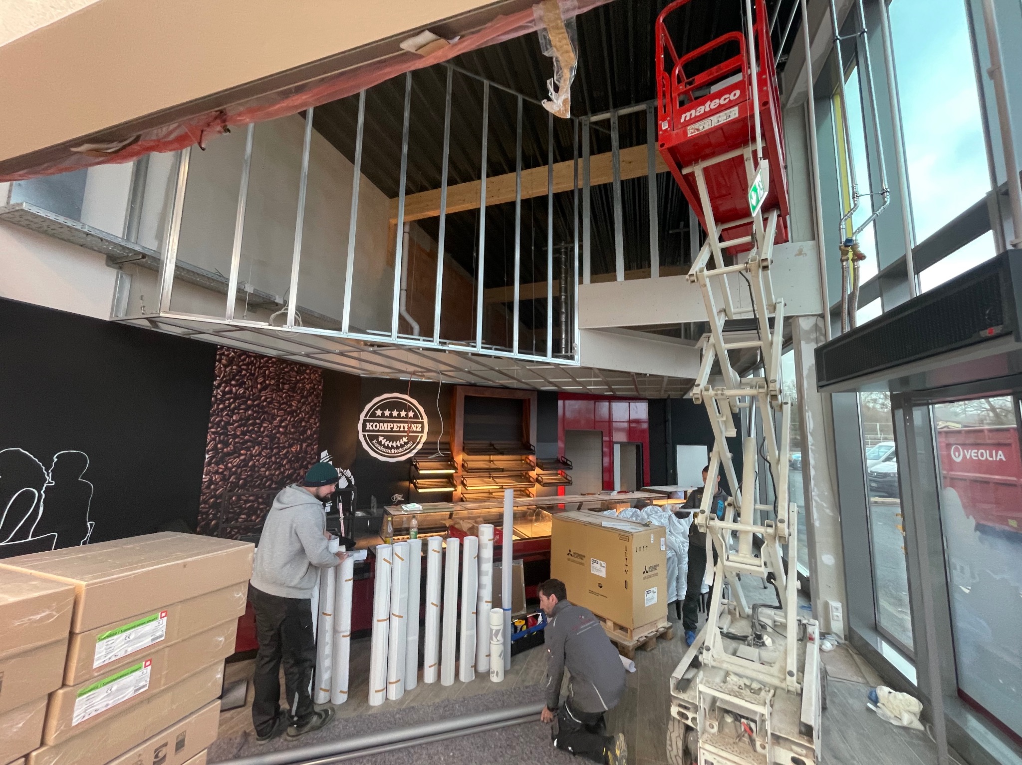 Montaż ścian działowych w lokalu komercyjnym: pracownicy układają profile, widoczny podnośnik i materiały budowlane. Etap prac wykończeniowych.