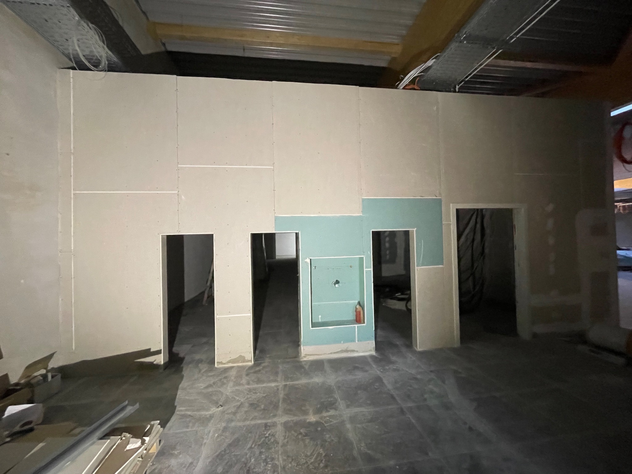 Montaż ścian działowych z płyt gipsowo-kartonowych z otworami na drzwi i wnęką, widoczne kable pod sufitem, surowy stan wykończenia.