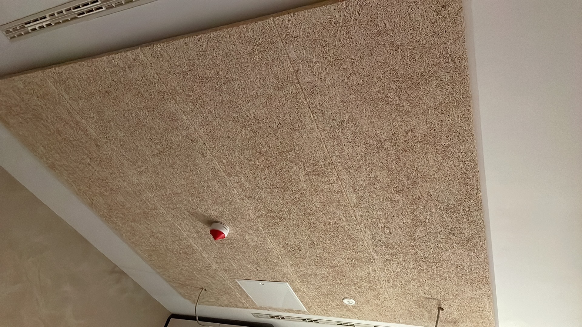 Zamontowany sufit z paneli z włókna drzewnego w jasnym odcieniu, widoczne detale faktury i łączenia paneli, z elementami instalacji sufitowej.