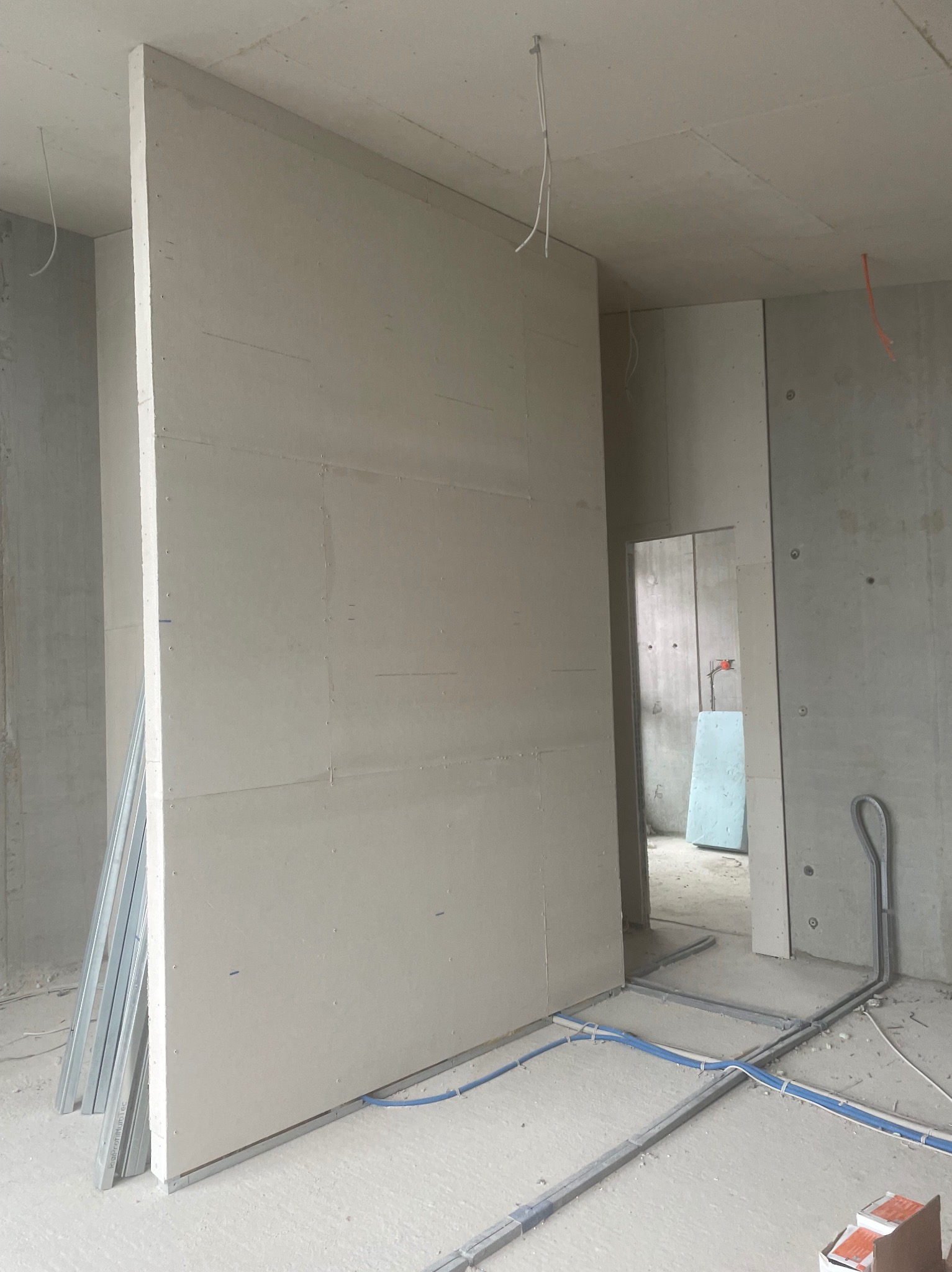 Montaż płyty karton-gips na metalowym stelażu w surowym wnętrzu. Widoczne przewody elektryczne i elementy konstrukcyjne. Ściana działowa w trakcie budowy.