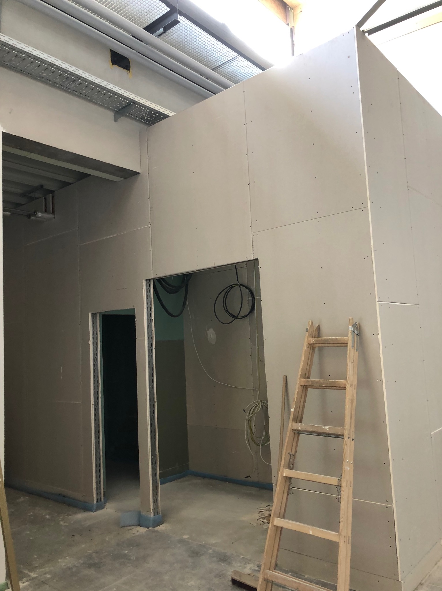 Wnętrze w trakcie prac z płyt karton-gips, widoczne profile i kable. Drewniana drabina oparta o ścianę. Surowy stan, przygotowanie do dalszych prac wykończeniowych.