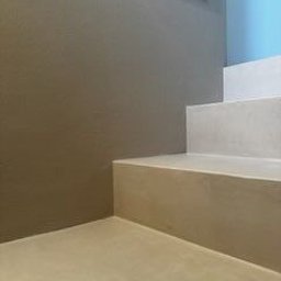 DZDekor - Minimalistyczne schody z mikrocementu w odcieniach beżu i szarości, z akcentem błękitu na ścianie. Gładka powierzchnia, nowoczesny design, widok z dołu, oświetlenie naturalne.