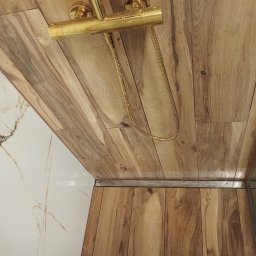DZDekor - Remont łazienki - Nowoczesna kabina prysznicowa w Szczecinie z płytkami imitującymi drewno, złotą baterią i odpływem liniowym, obok białych płytek marmurowych.