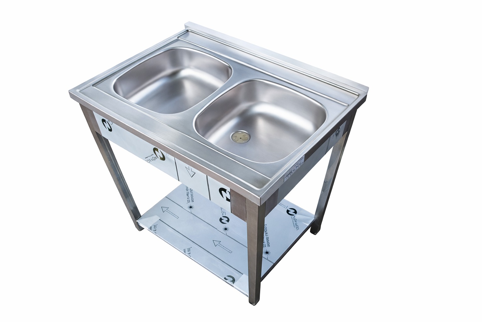 Stalowy zlew dwukomorowy na metalowym stelażu z półką, widok z góry pod kątem. Zlew o prostych kształtach, z widocznymi elementami montażowymi i folią ochronną.