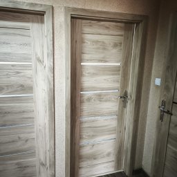 4Trade Paweł Milik - Zamknięte, drewnopodobne drzwi wewnętrzne z poziomymi, srebrnymi wstawkami, widoczne w kadrze obok innych drzwi o podobnym designie, na tle teksturowanej ściany.