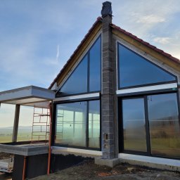 4Trade Paweł Milik - Nowoczesny dom z dużymi oknami aluminiowymi, widok z zewnątrz, w tle krajobraz. Widoczne rusztowanie i elementy konstrukcyjne w trakcie budowy.