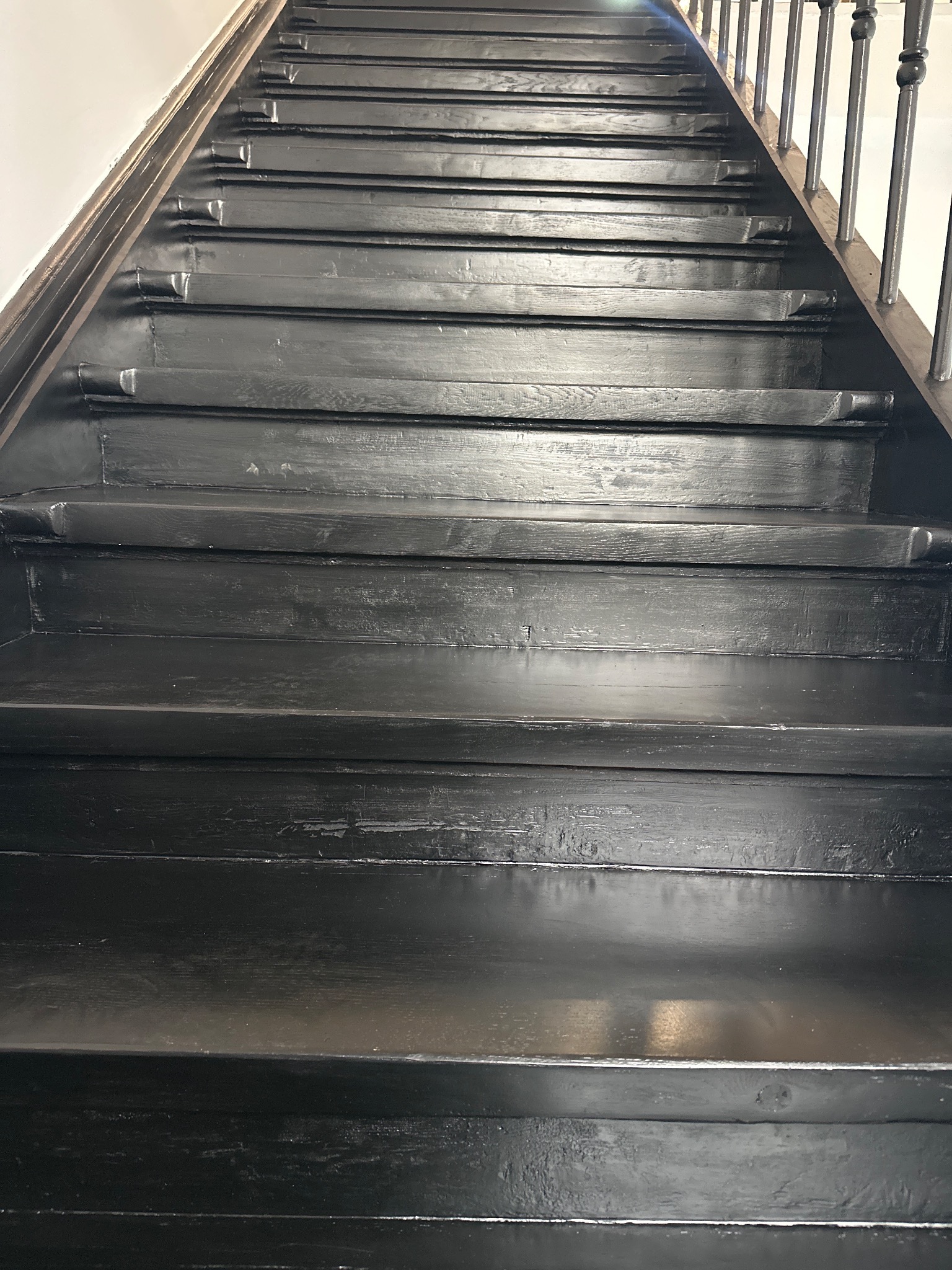 Pomalowane na czarno drewniane schody w domu w Warszawie. Widok z dołu, ukazujący detale stopni i poręczy. Renowacja schodów.