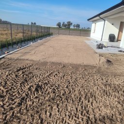 Automatyczne nawadnianie ogrodów.Marcin Chądzyński - Przygotowany teren pod trawnik przy domu jednorodzinnym. Widoczne ślady opon i wyrównana powierzchnia piasku. W tle ogrodzenie i zieleń.