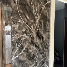 MTM Renowacje - Ściana z dekoracyjną, czarno-białą fakturą przypominającą marmur z białymi żyłkami, widoczna z bliska, z fragmentem futryny drzwiowej i wnętrza w tle.