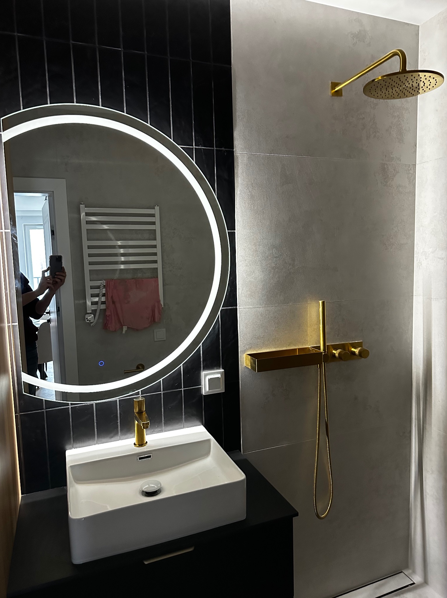 Nowoczesna łazienka w Białymstoku z czarno-białymi płytkami, okrągłym lustrem z podświetleniem LED i złotą armaturą. Minimalistyczny design.