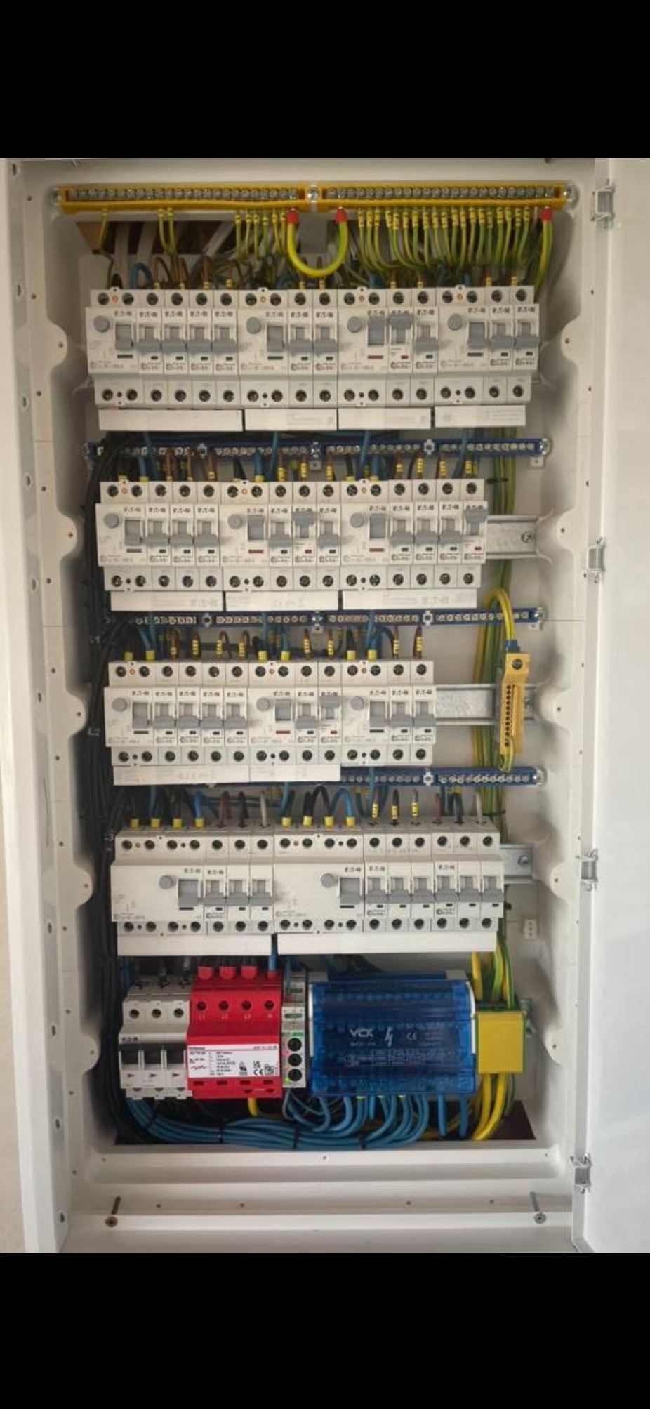 Rozdzielnica elektryczna w białej obudowie, widoczne zabezpieczenia, przewody i listwy. Starannie wykonana instalacja.