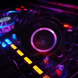 SAVART Events Oleksandr Sava - Profesjonalny mikser DJ z słuchawkami, podświetlony neonowym światłem. Widoczne suwaki, pokrętła i przyciski. Sprzęt gotowy do występu na żywo.