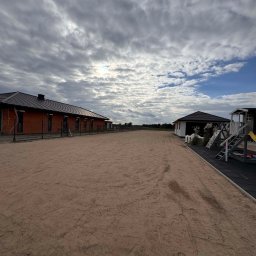 Trawtex - Rozległy teren z piaskowym podłożem, otoczony budynkami i ogrodzeniem. Ślady na piasku sugerują niedawne prace ziemne lub przygotowanie terenu pod inwestycję.