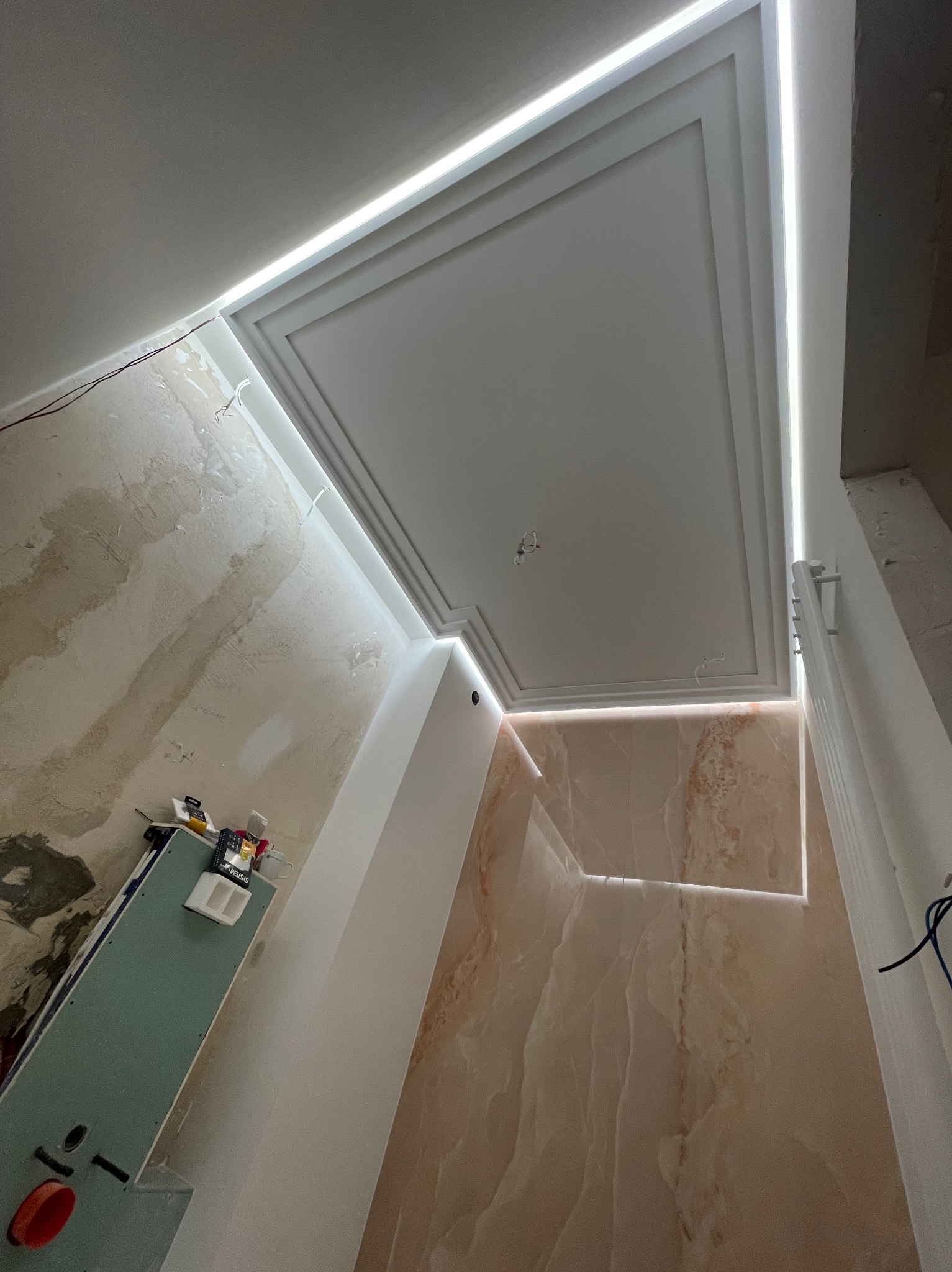 Kaseton sufitowy z oświetleniem LED w trakcie montażu. Widoczne niedokończone ściany i narzędzia. Ujęcie z dołu, podkreślające detale wykończenia.