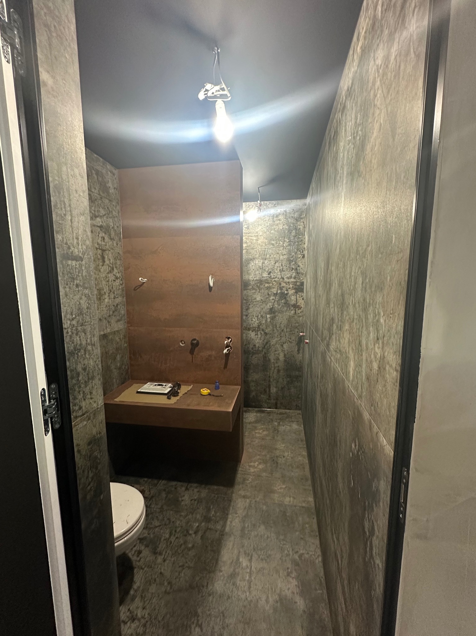 Nowoczesna łazienka w trakcie wykańczania: surowe ściany, podwieszana umywalka z narzędziami, widoczna instalacja oświetleniowa. Minimalistyczny design.