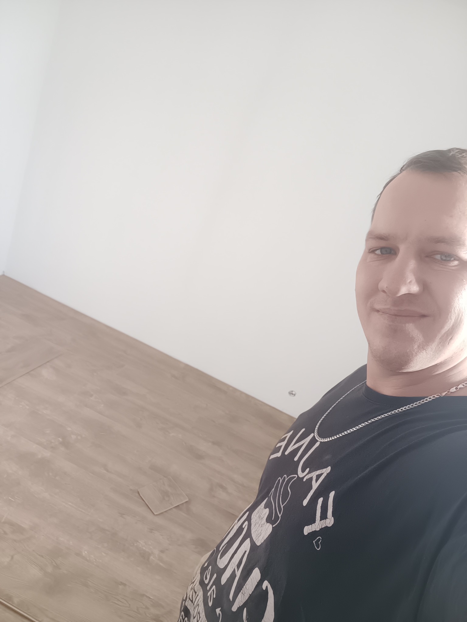 Ukończona podłoga z paneli w jasnym odcieniu drewna, widoczna z perspektywy osoby stojącej w rogu pomieszczenia. Białe ściany, naturalne światło.