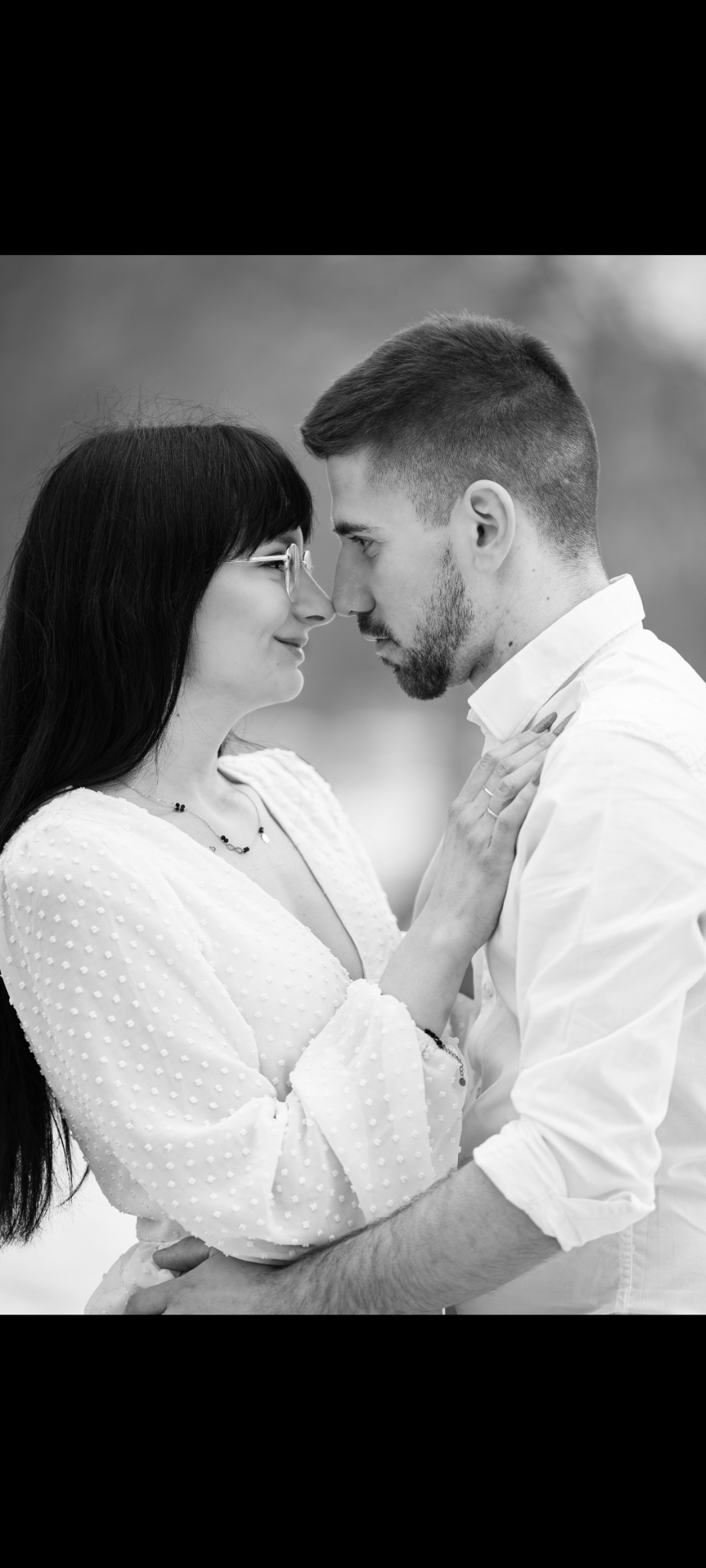 Czarno-białe zbliżenie na parę, dotykającą się nosami. Kobieta w okularach i wzorzystej sukience, mężczyzna w białej koszuli. Delikatne światło, romantyczny nastrój.