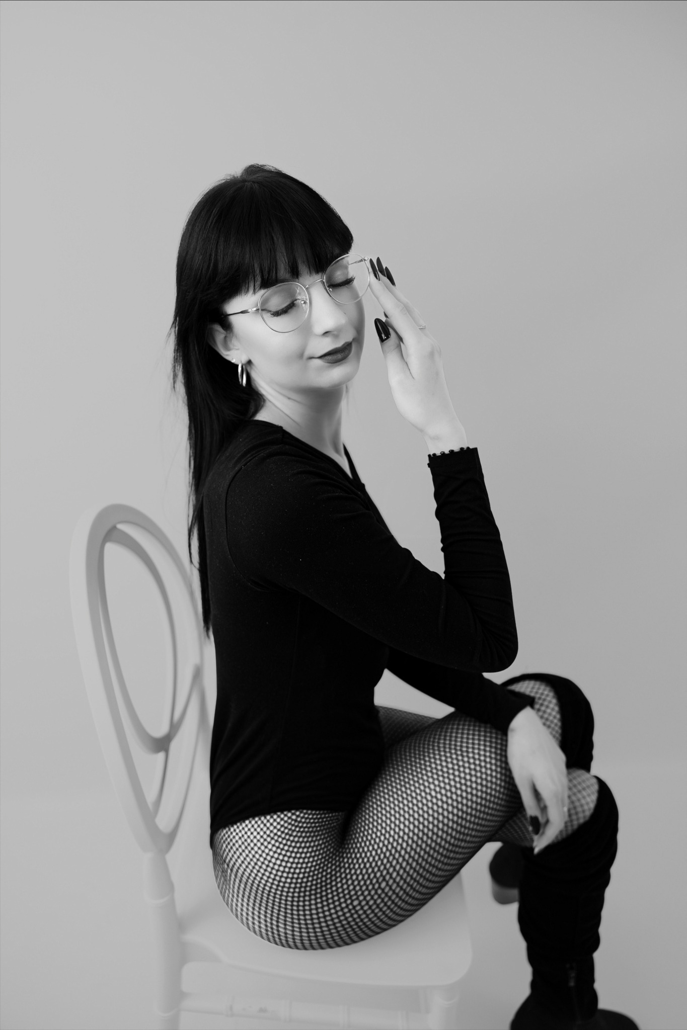 Czarno-białe zdjęcie kobiety w okularach, siedzącej na krześle w Kraszkowicach. Ubrana w czarny strój i kabaretki, z ręką przy okularach i zamkniętymi oczami.