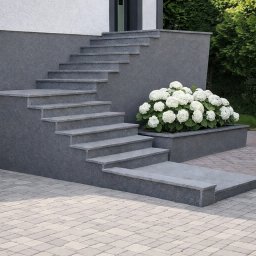 GlamourStone - Zewnętrzne schody z szarego kamienia prowadzą do drzwi wejściowych. Obok schodów rosną białe hortensje w kamiennej donicy. Brukowana ścieżka prowadzi do schodów.
