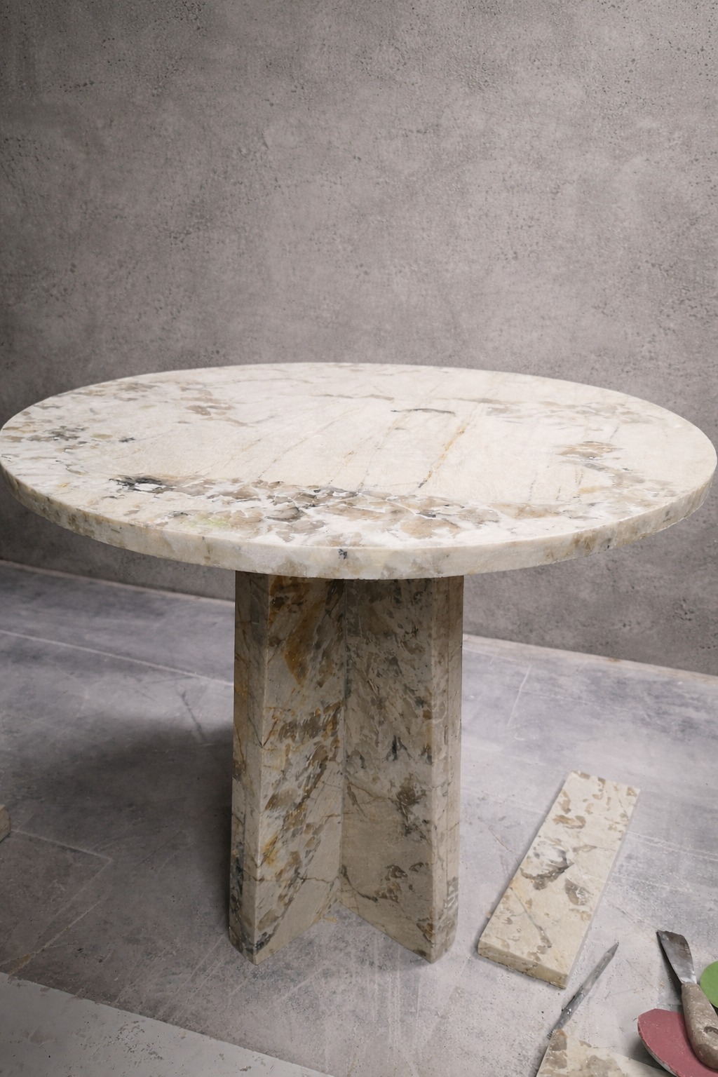 Okrągły blat kamienny na geometrycznej podstawie z tego samego materiału. Obok leżą fragmenty kamienia i narzędzia kamieniarskie. Szlifowanie blatu kamiennego.