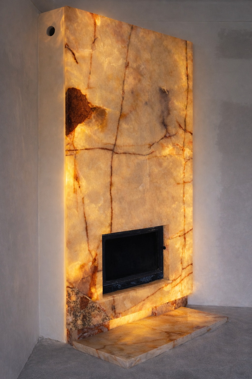 Podświetlony, okładzinowy kominek z onyksu z czarnym wkładem, ukazujący unikalny wzór kamienia i ciepłe oświetlenie w surowym wnętrzu.