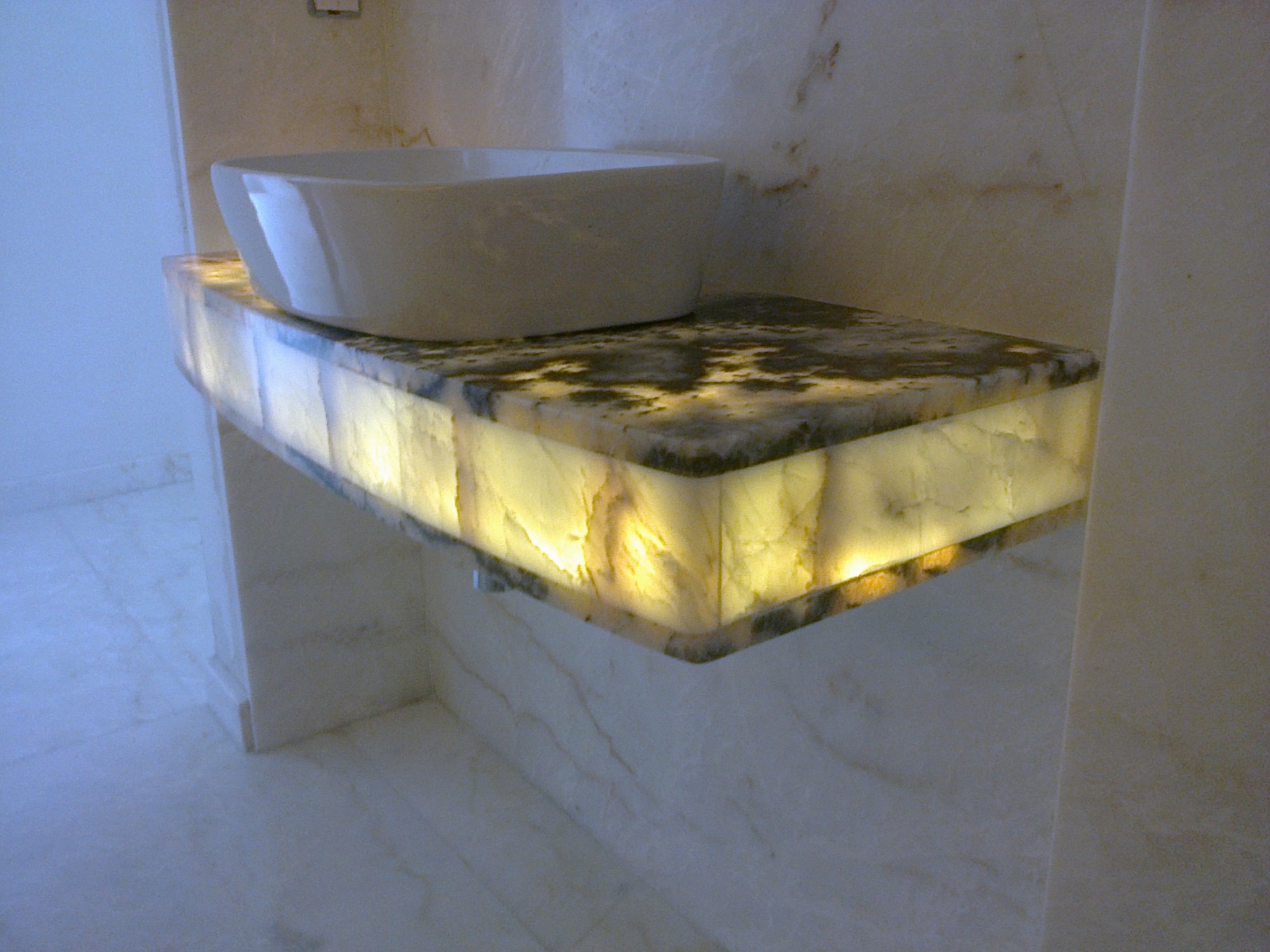 Podświetlany blat z kamienia onyksowego w łazience, z umywalką nablatową. Ciepłe światło podkreśla unikalny wzór kamienia. Minimalistyczny design.