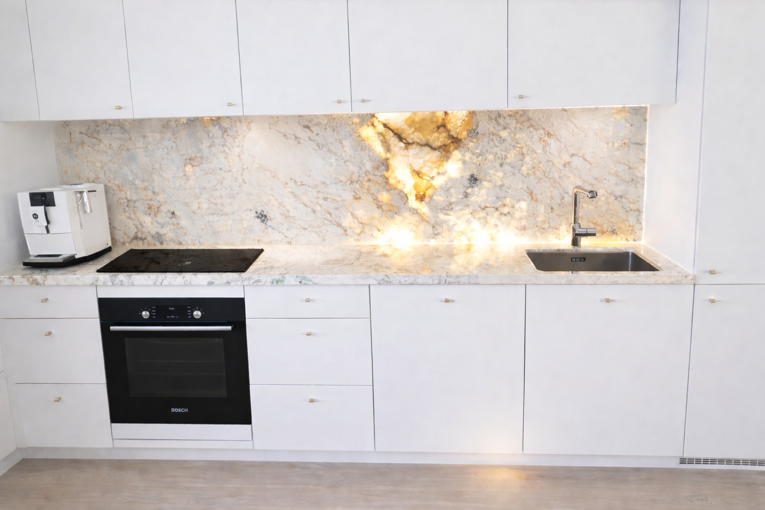 Biała kuchnia z blatem kamiennym o unikalnym wzorze, podświetlonym od spodu. Widoczny zlew, płyta indukcyjna i ekspres do kawy. Minimalistyczny design.