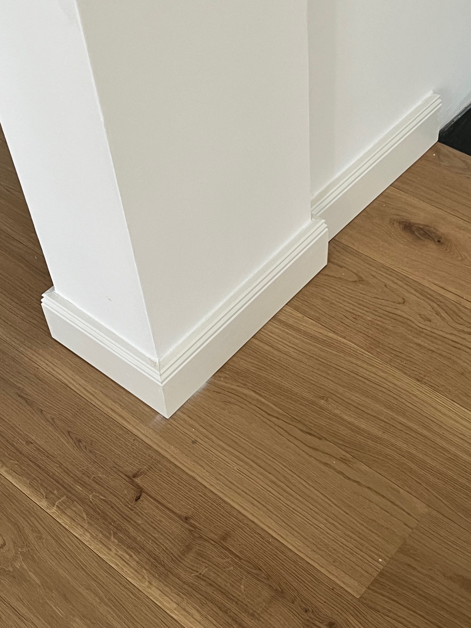 Jasne panele podłogowe ułożone przy białej ścianie z listwami przypodłogowymi. Detal wykończenia wnętrza, widok z góry.