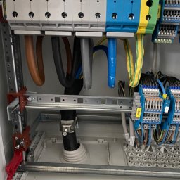ProfiMajster usługi elektryczne - Wnętrze szafy elektrycznej z uporządkowanymi przewodami zasilającymi, kolorowymi listwami zaciskowymi i szynami DIN, gotowe do podłączenia obwodów.
